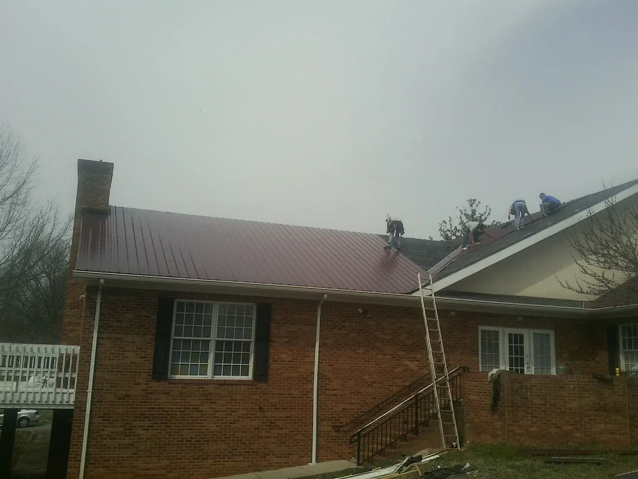 Crew setting red metal roofing panels on a brick home in Manning