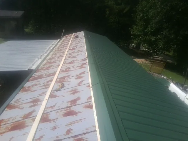 Old rusted panels beside newly installed green metal roofing — Wind Damage Roof Repair by Roofing Brothers in Manning